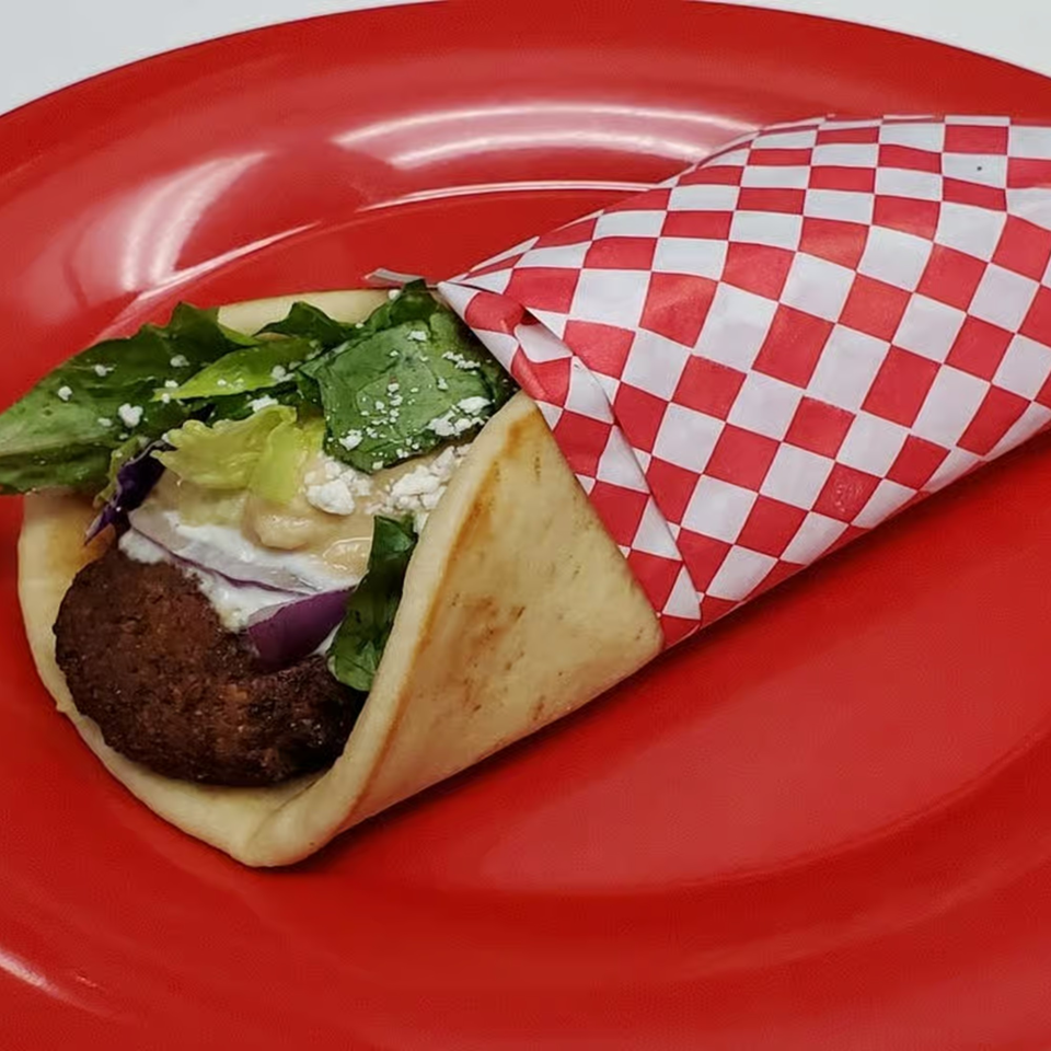 A Gyros And More falafel gyro, wrapped in checkered paper, on a red plate.